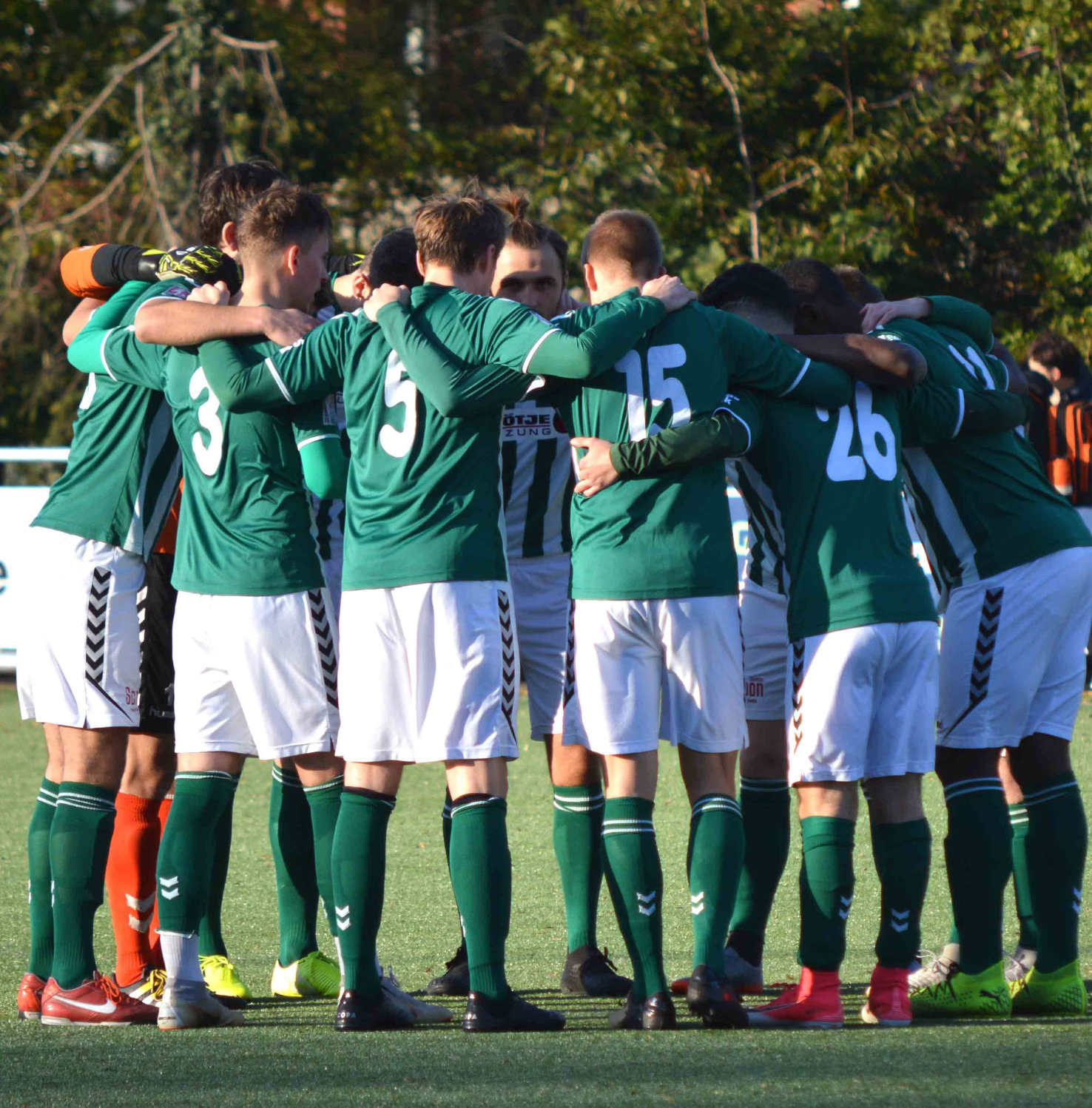Soccer team in green jerseys and white shorts huddle on the field before a game.
