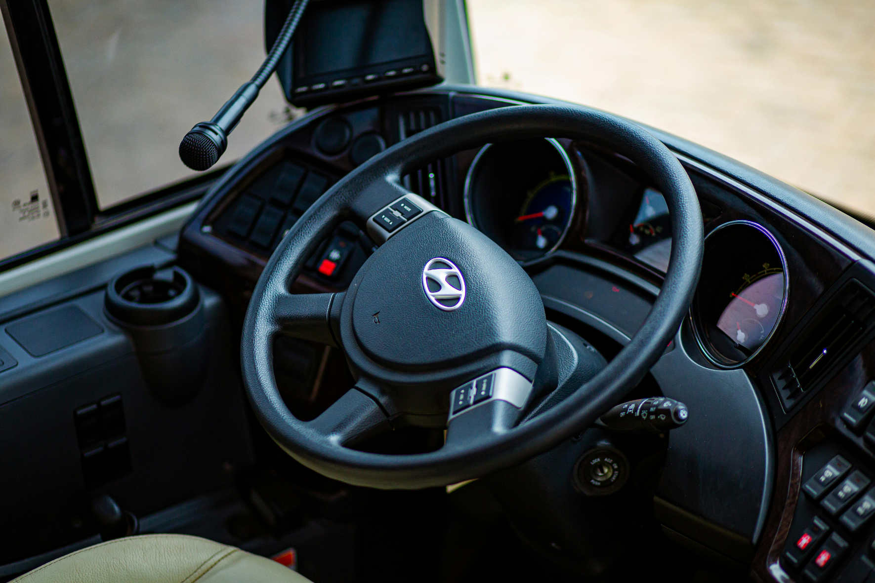 Steering wheel and dashboard inside a Hyundai vehicle showing controls, gauges, and a microphone.