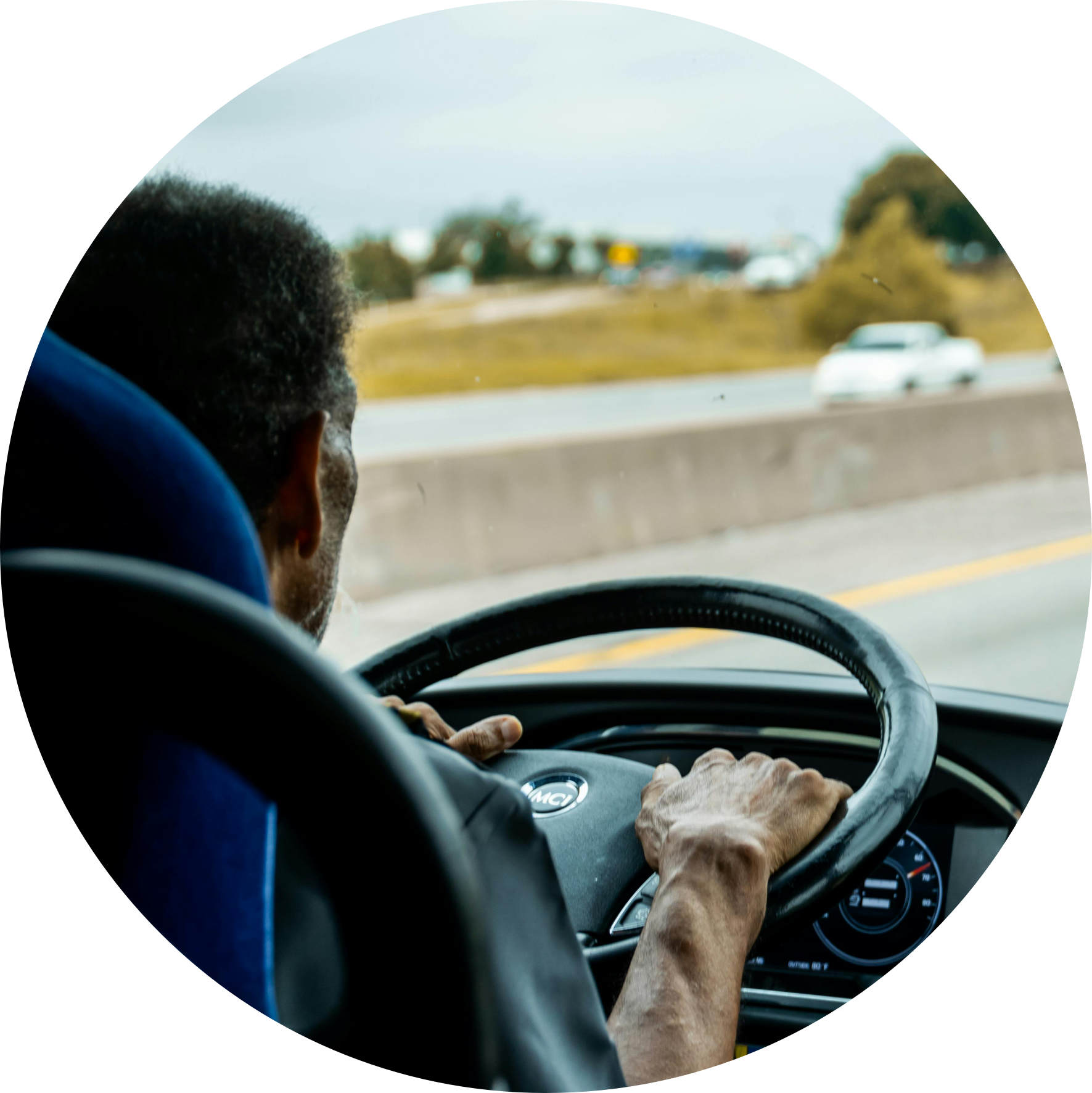 Man driving a vehicle on a highway, hands on the steering wheel, view from inside the vehicle.